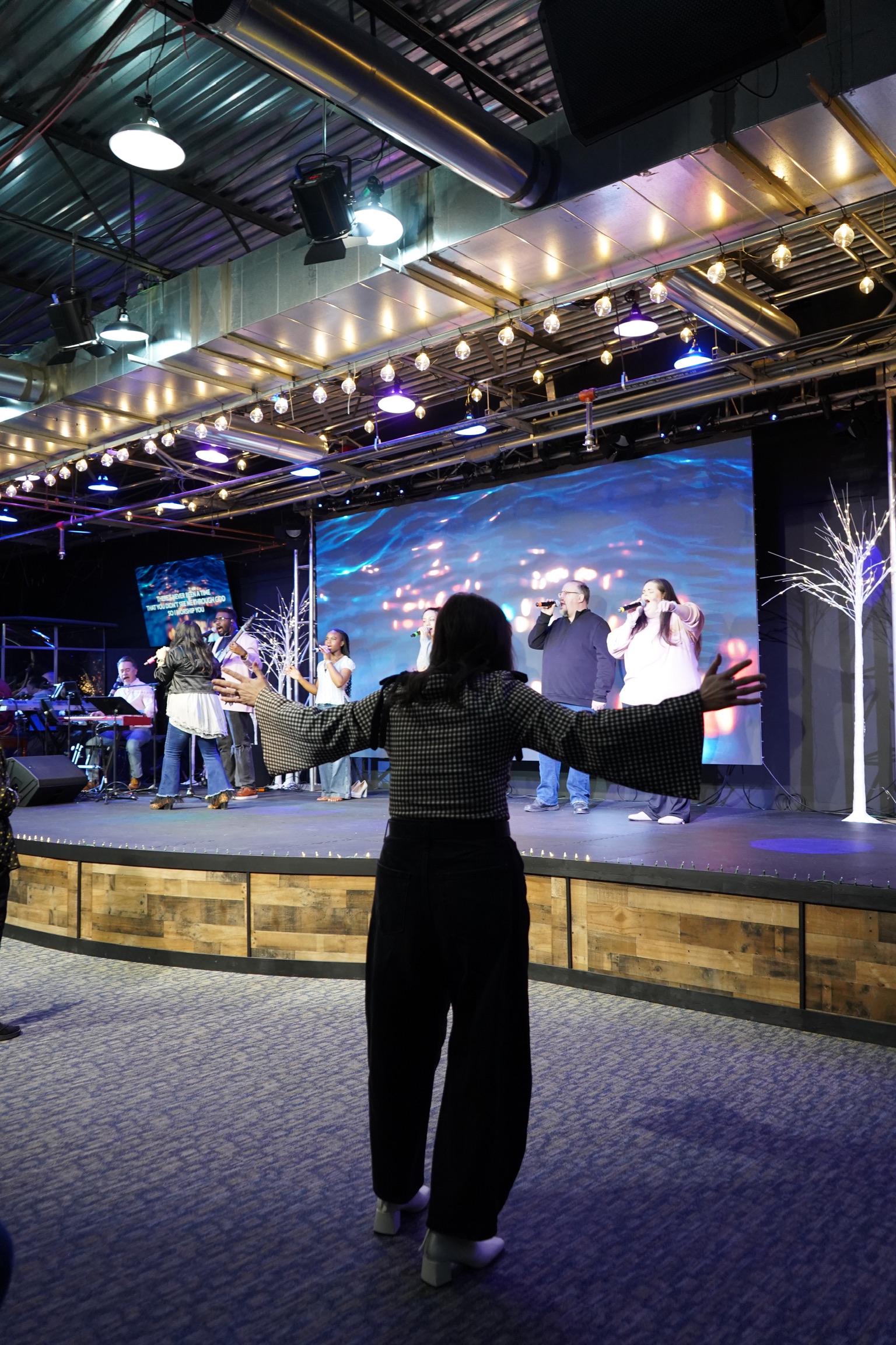 A worshipper facing the worship team with arms open.