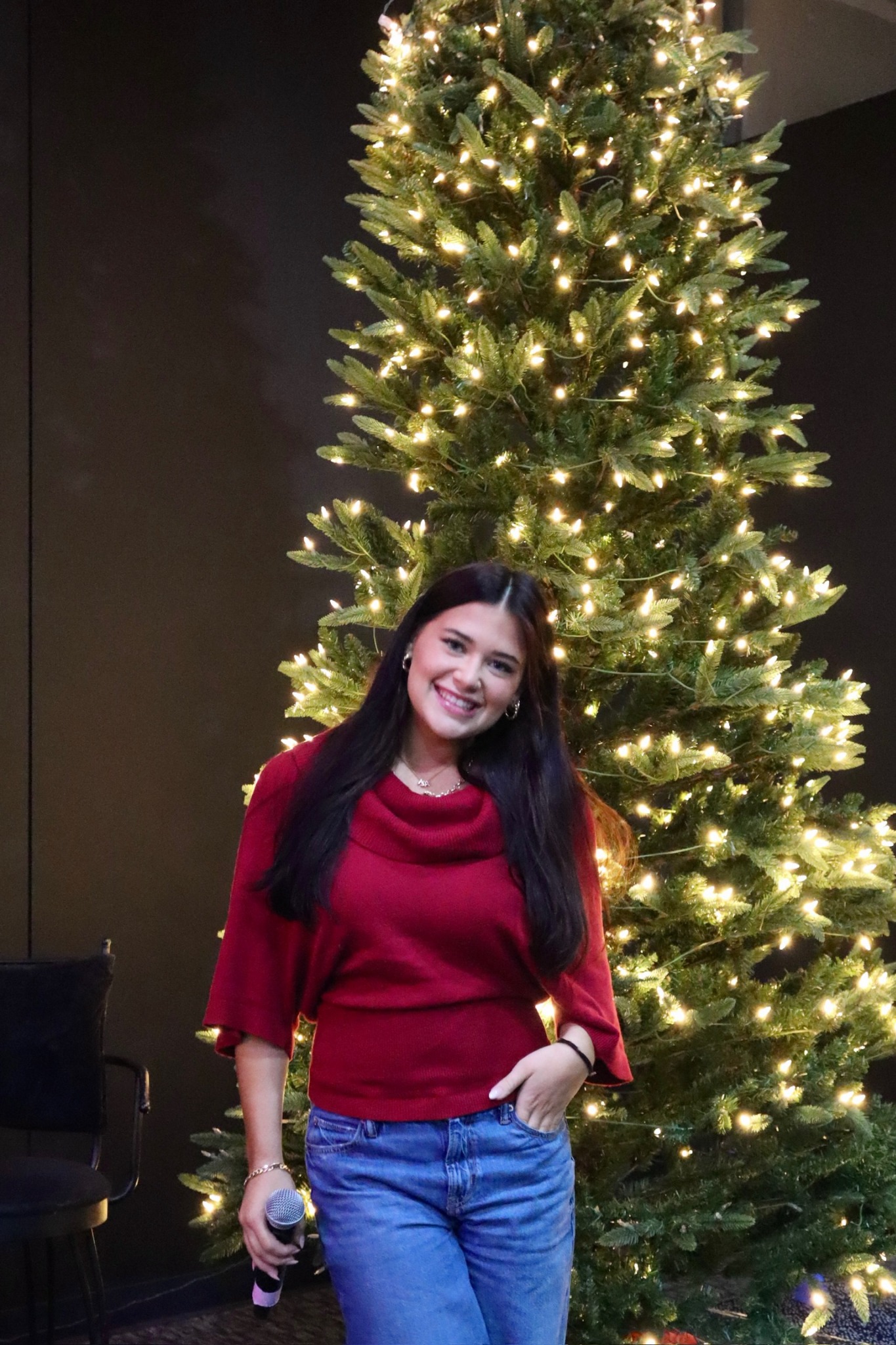 A young adult holding a microphone beside a Christmas tree at Bethesda.