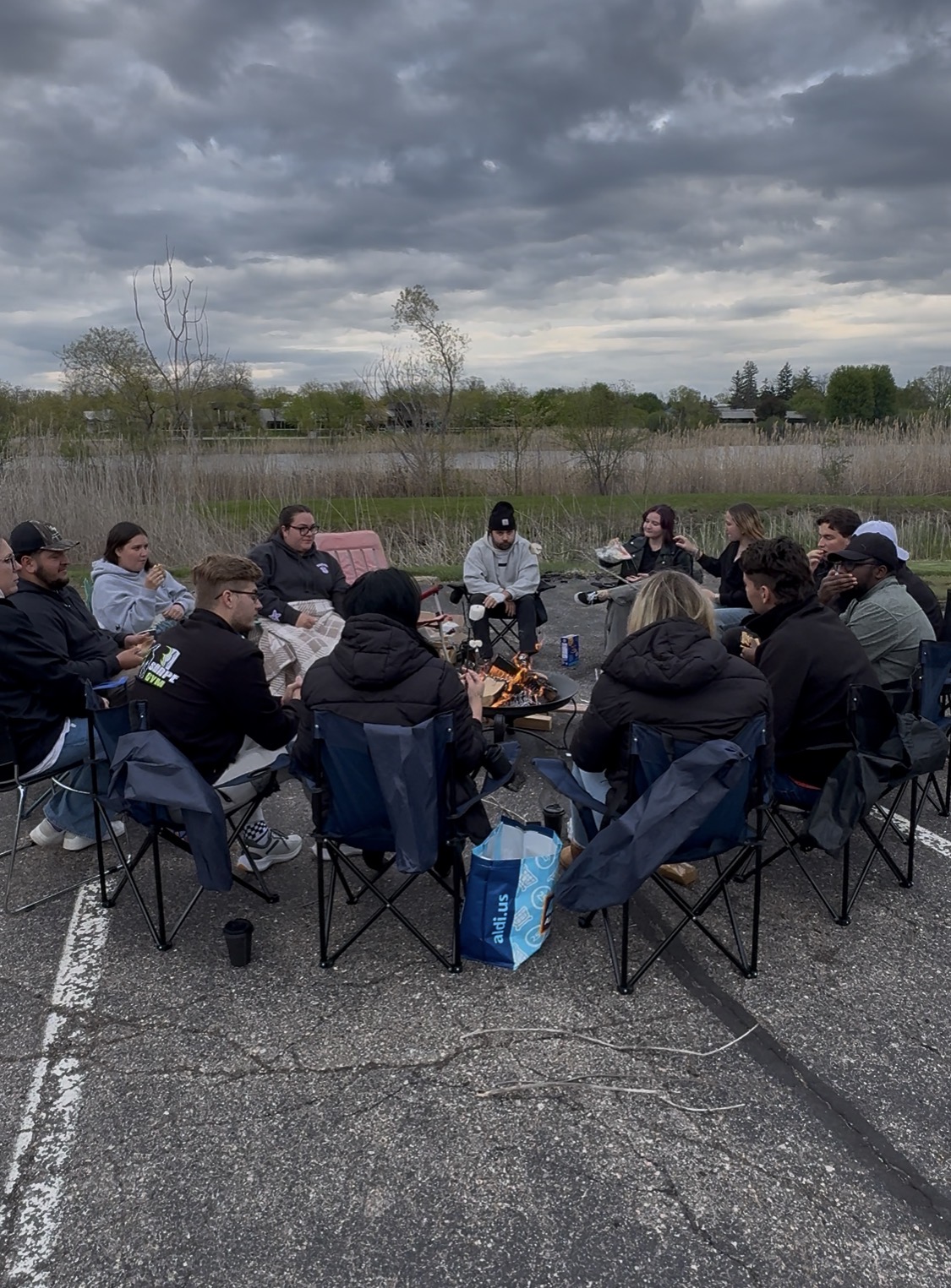 Young adults gathered around an outdoor fire for conversation.